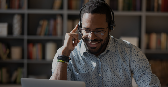 Focused African man sitting at desk wear headset watching webinar video course gain new knowledge use on-line application website. Manager talk to client provide professional help and support concept