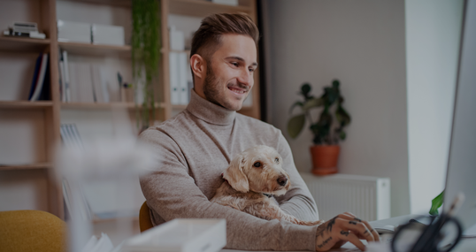 Young businessman with dog sitting at the desk indoors in office, using computer.